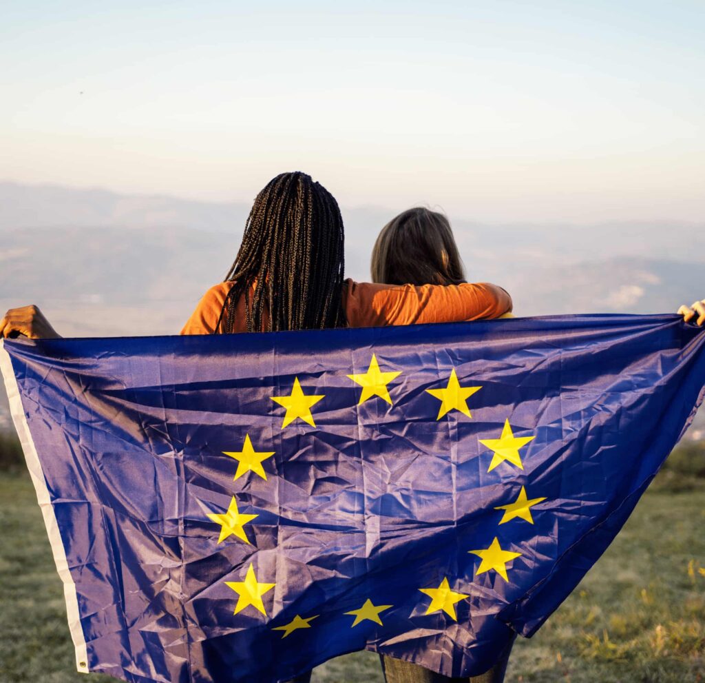 Zwei Frauen halten die EU Flagge und schauen in die Ferne.