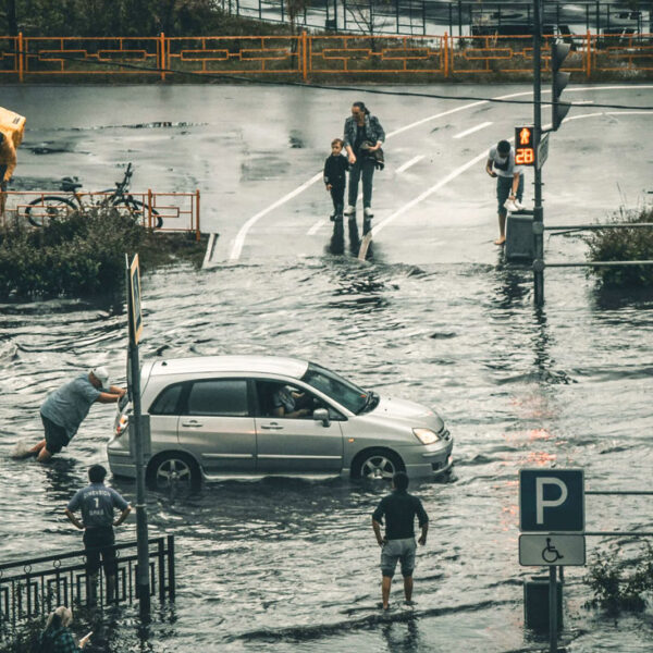 Eine Straße steht unter Wasser. Ein Mann versucht sein Auto von der überfluteten Straße zu schieben.