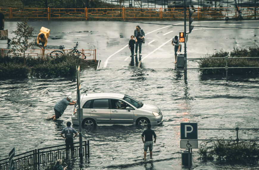 Eine Straße steht unter Wasser. Ein Mann versucht sein Auto von der überfluteten Straße zu schieben.